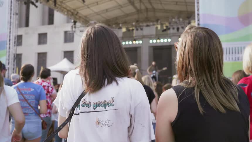 Two white females sway and sing along with a band at an outdoor concert