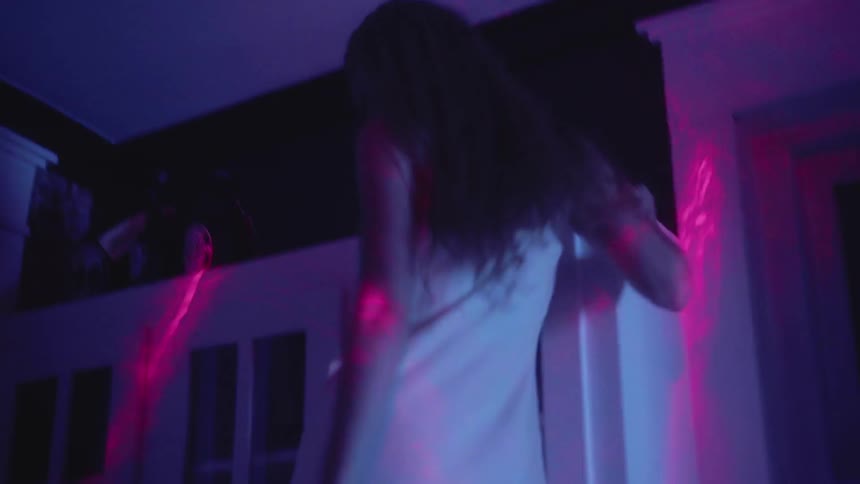 A woman in a nightgown dances on a kitchen counter in pink light
