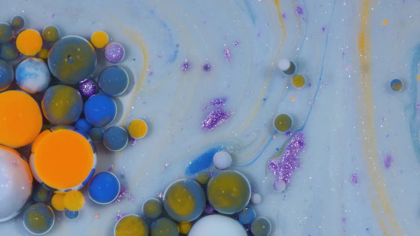 Brightly colored paint drops floating on a milky substance with glitter