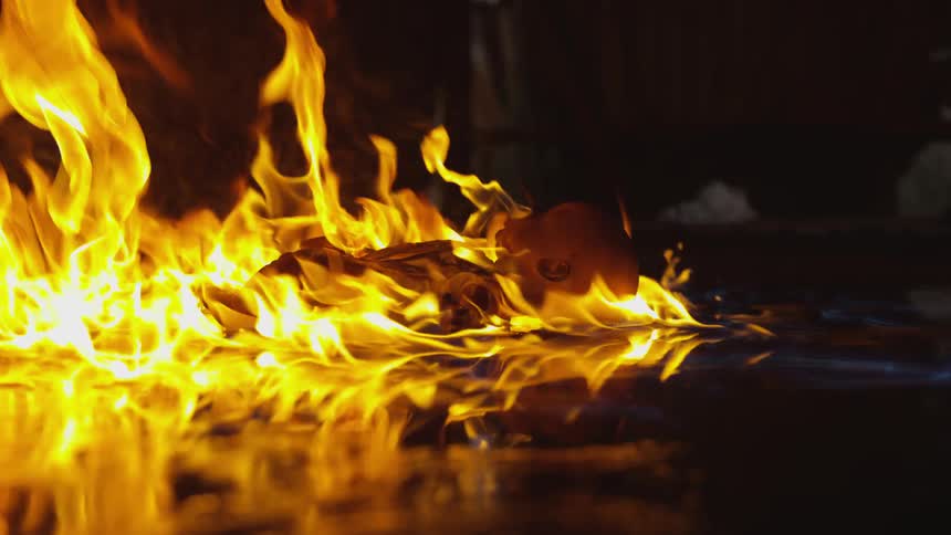 A fire consumes a doll on a floor