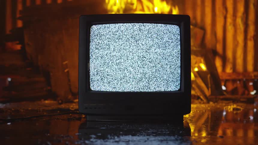 A fire burns behind a television displaying static