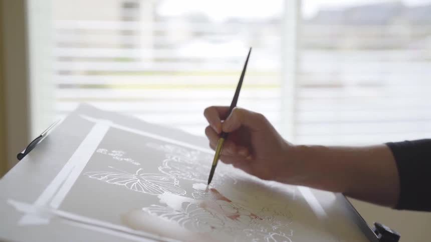 An artist uses a brush to paint using a stencil on canvas