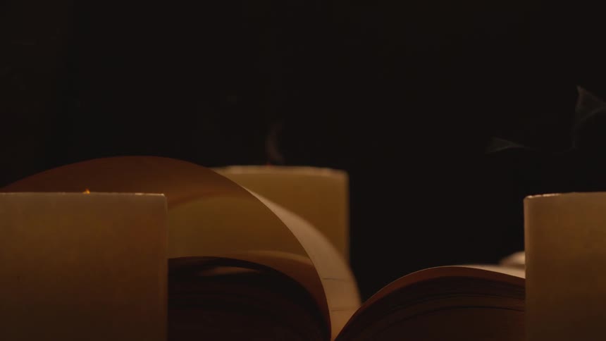 A book page turning in the wind surrounded by three lit candles