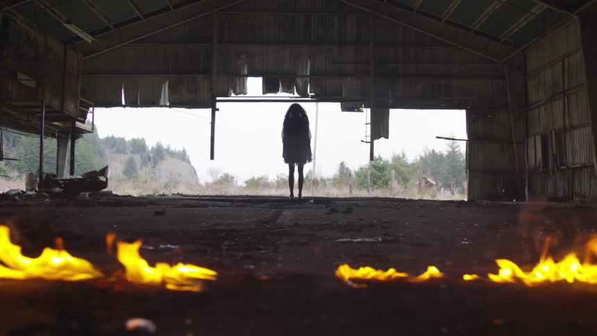 A woman stands in the dark abandoned building with a line of fire