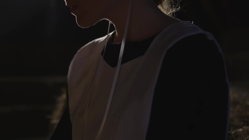 A woman sitting in a dimly lit barn