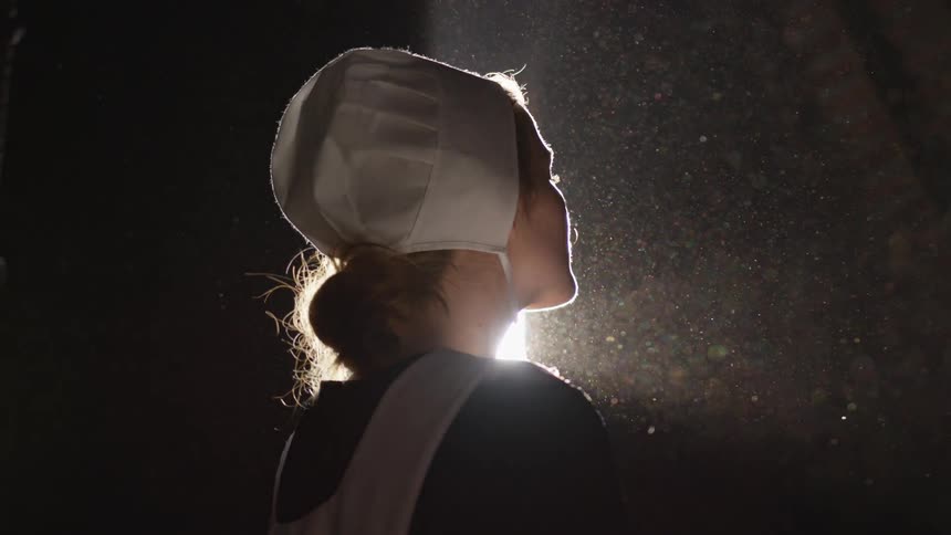 Woman stands in dark building while the sun shines on her face