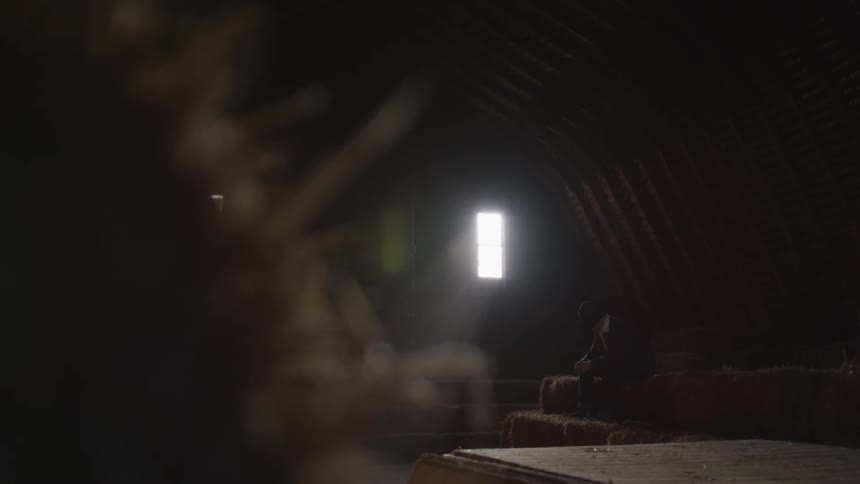 Man sits with head bowed on hay bales in barn