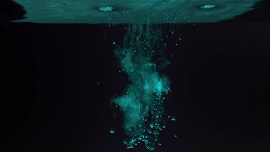 A blue cloud flows, drips and sinks down into black liquid from the surface