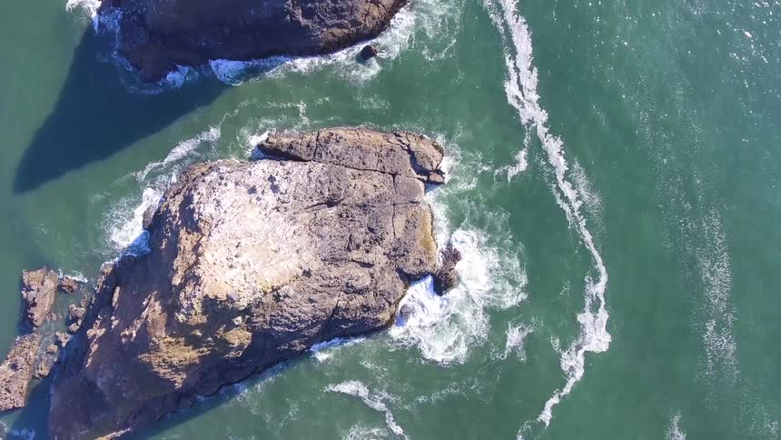 The rough waters crash against the rocks on a sunny day