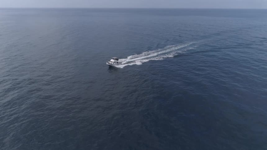 A boat powers through vast but calm ocean waters