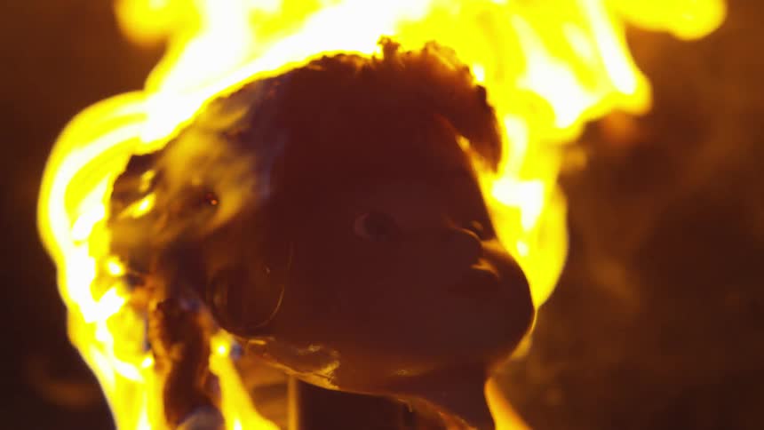 Fire engulfs a doll's head and it melts