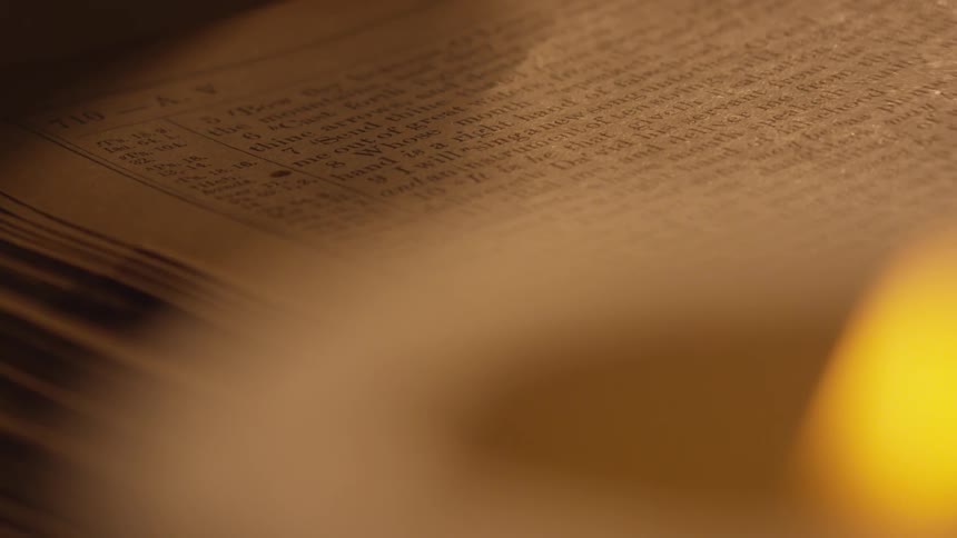 A burning candle illuminates the page of a book