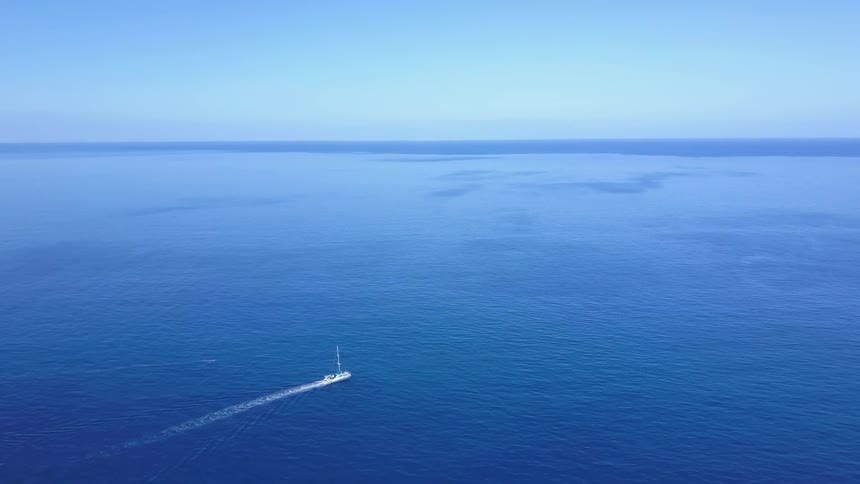 A boat with a mast leaves a wake in the blue ocean