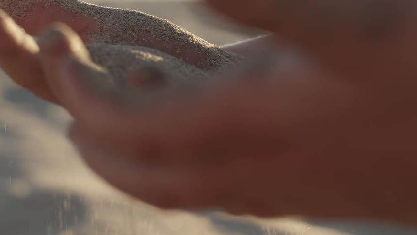 Sand sifting through a woman's hands on the beach
