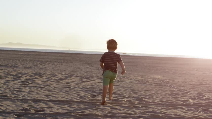 A boy runs across the sand to the water on a sunny day