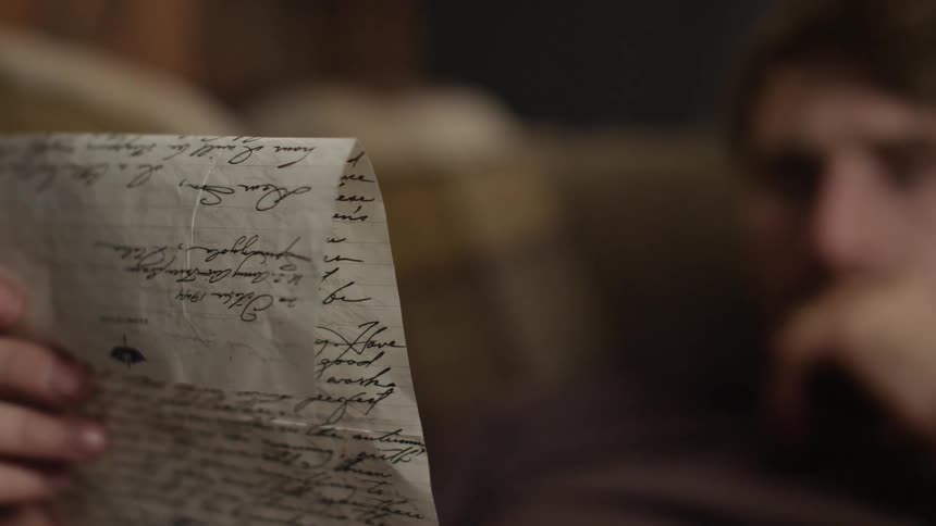 Man sits indoor reading a handwritten letter