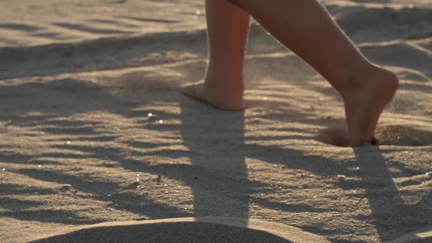 Barefoot youngster walking through a large sandy area