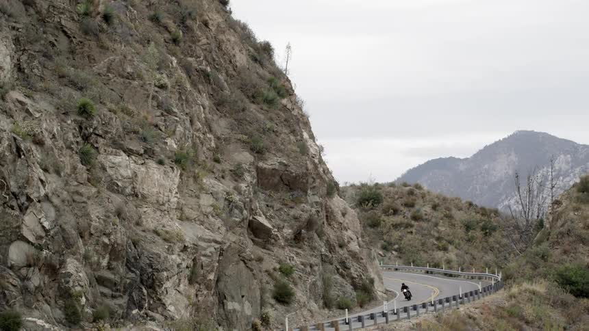 Small road by a mountain as one motorcycle passes