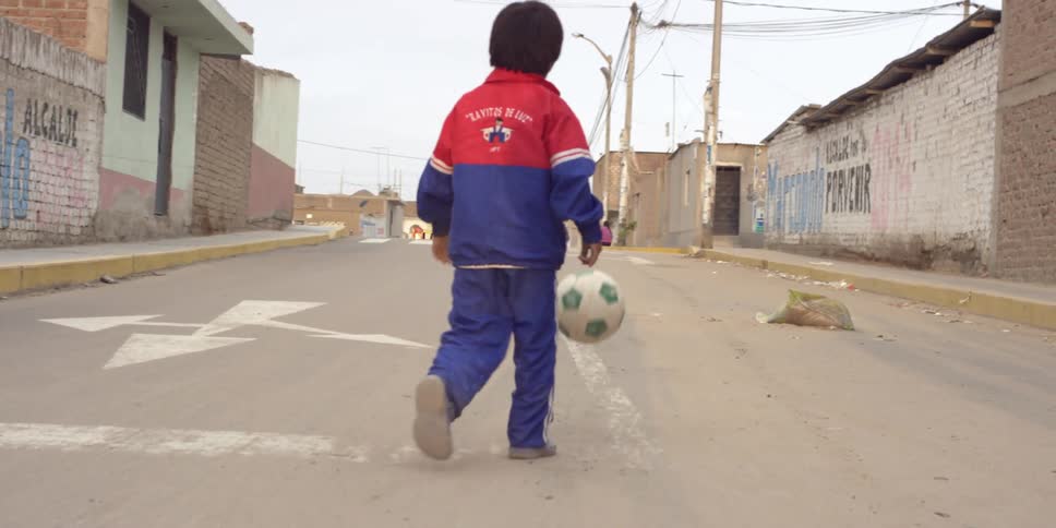 Young boy playing with his soccer ball on a slow street