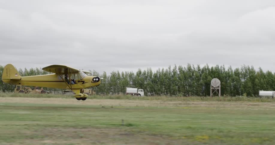 Small crop duster plane takes off in a field on an overcast day