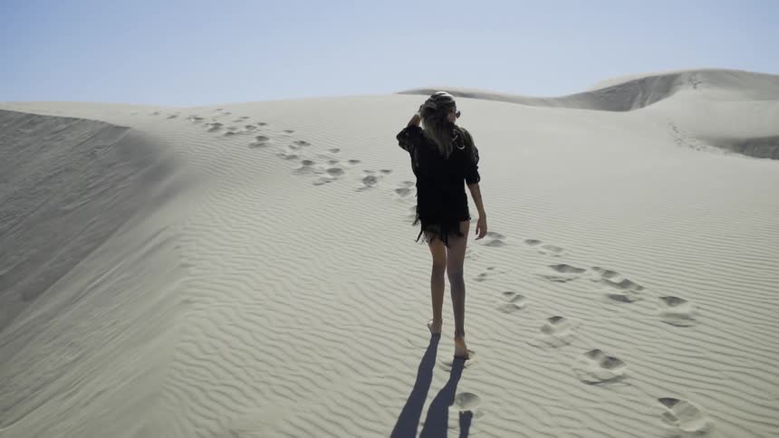 Woman walks on a sand dune in the desert on a sunny day