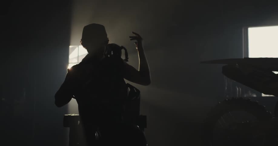 A man putting on a backpack with light shining in the window behind him