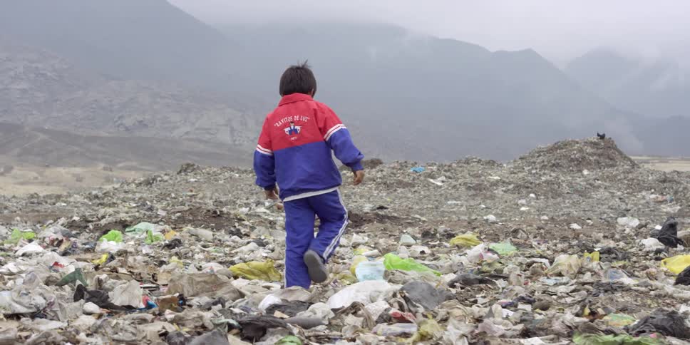 A child walks along a rocky mound covered in trash
