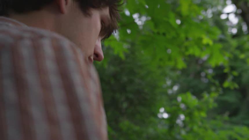 A young man walks through a forested area with a fairly dense canopy