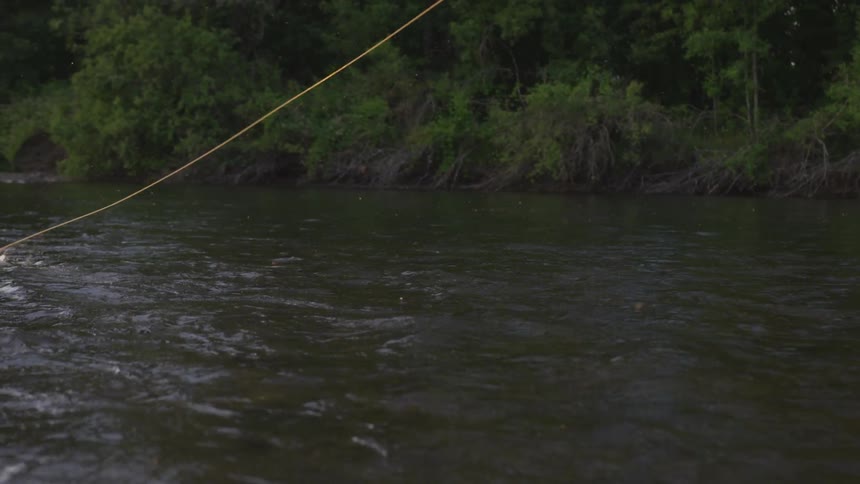 A long fishing line that is being pulled along in a swiftly flowing river is pulled out of the water