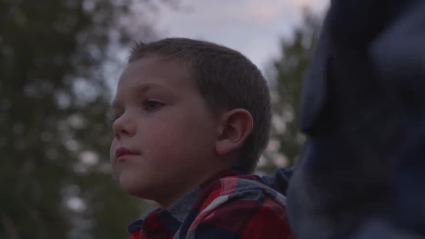 A child standing next to another person outdoors in a forest