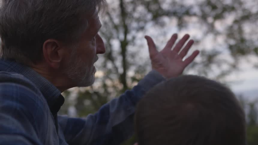 A dad talks to his son then gestures up to the sky and trees