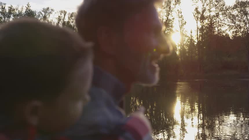 Father and son stand on lakes shore as son points things out with trees on the opposite shore