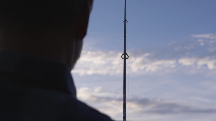 A man holds a fishing rod against a blue sky