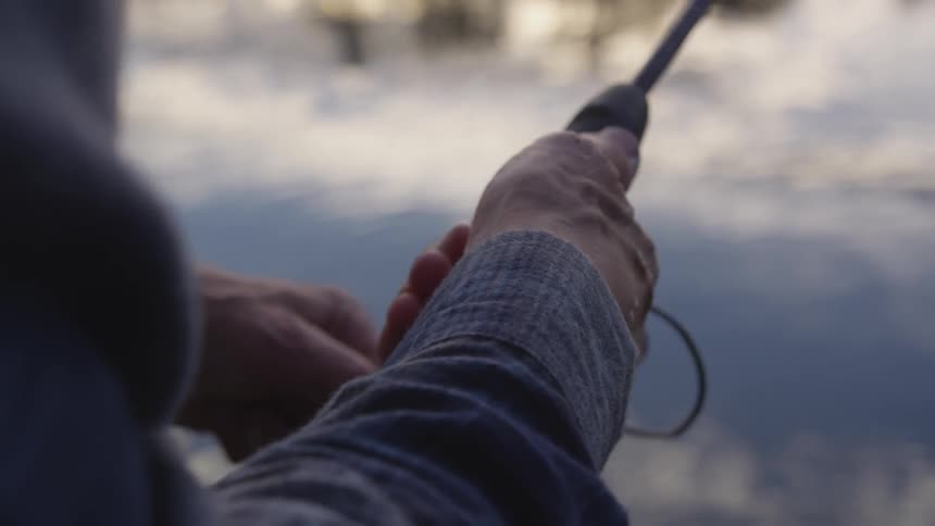 Man fishes with his fishing rod by the tranquil lake at dusk