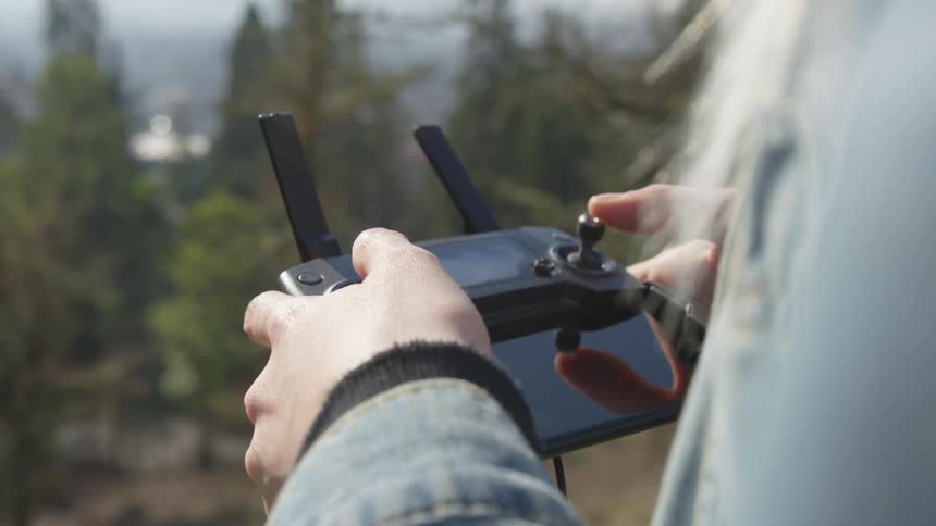 Man stands outside near trees manipulating drone controller