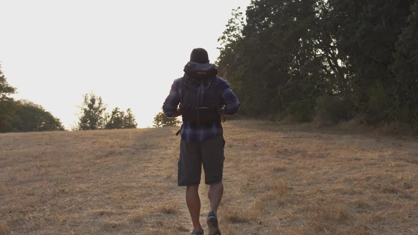 Man with backpack walks through short brown grass