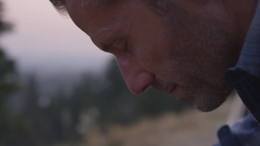 Man bows head and closes eyes outside