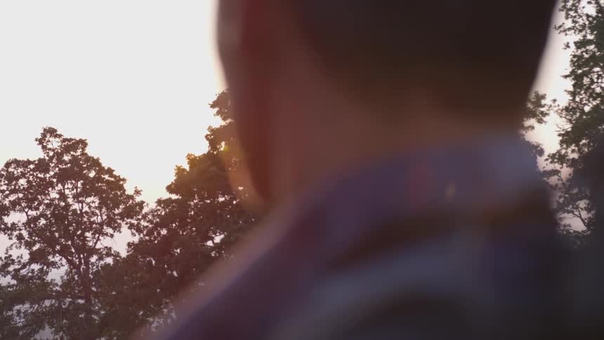 A man carrying a backpack watches the sun rise over some trees
