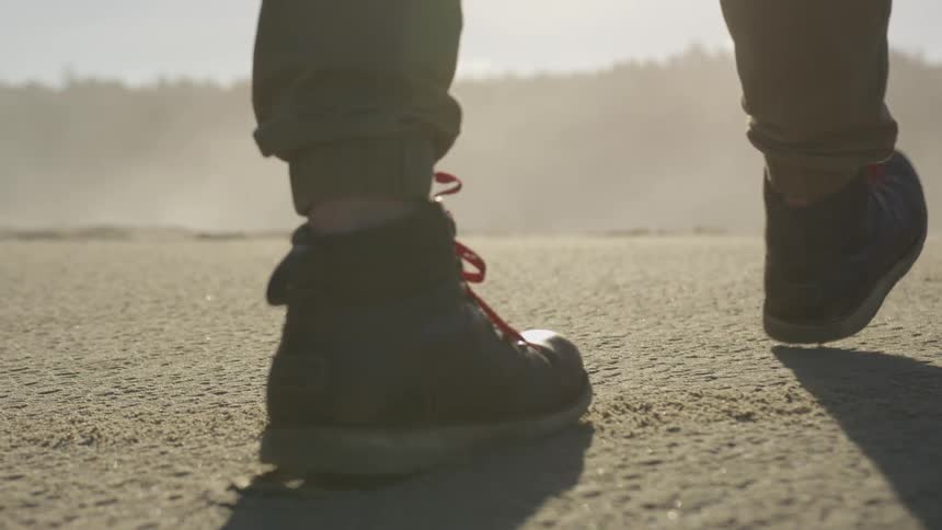 A person walking across a sandy area while wearing boots