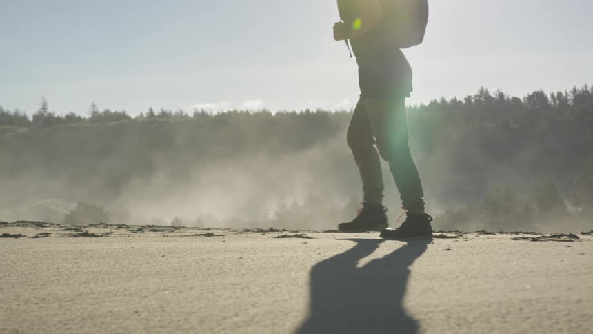 A man carrying a backpack hikes a dirt path at a high elevation with a forest in the distance