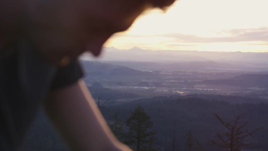 A tired man resting on a hill or mountain top at sunset