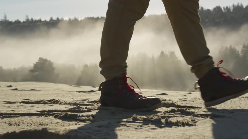 A person walks in a foggy desert at sunrise