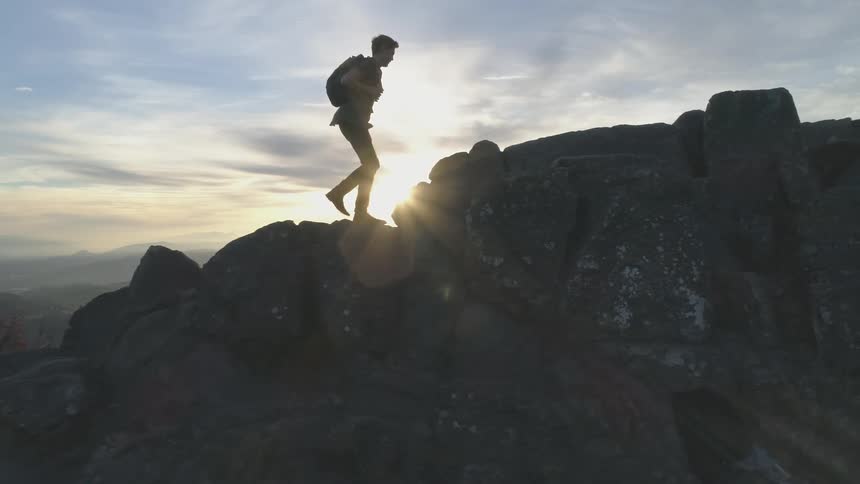 Man walks up rocks at sunset