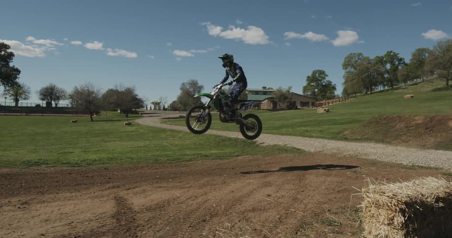 A man on a motorcycle lands after making a jump at the bottom of a grassy hill