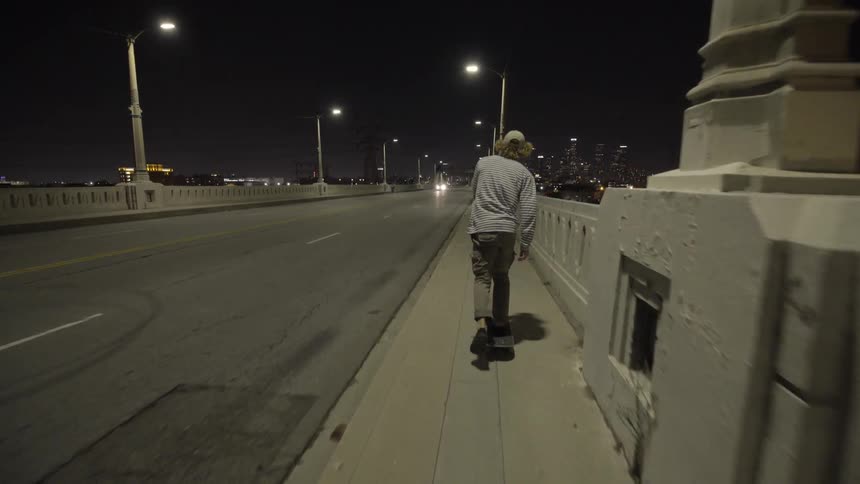 A man skateboarding across a city bridge at night