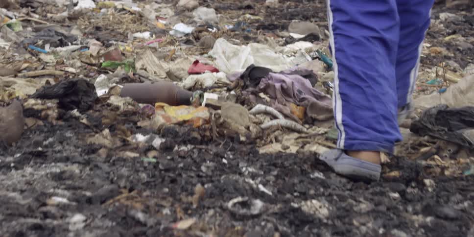 Close up of a boy's feet and legs as he walks through a landfill