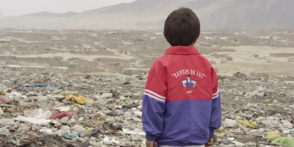 A boy looking out at a rocky landscape littered with trash