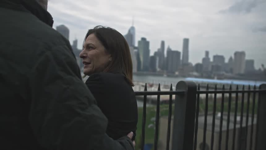 A couple stand talking with city skyline in background