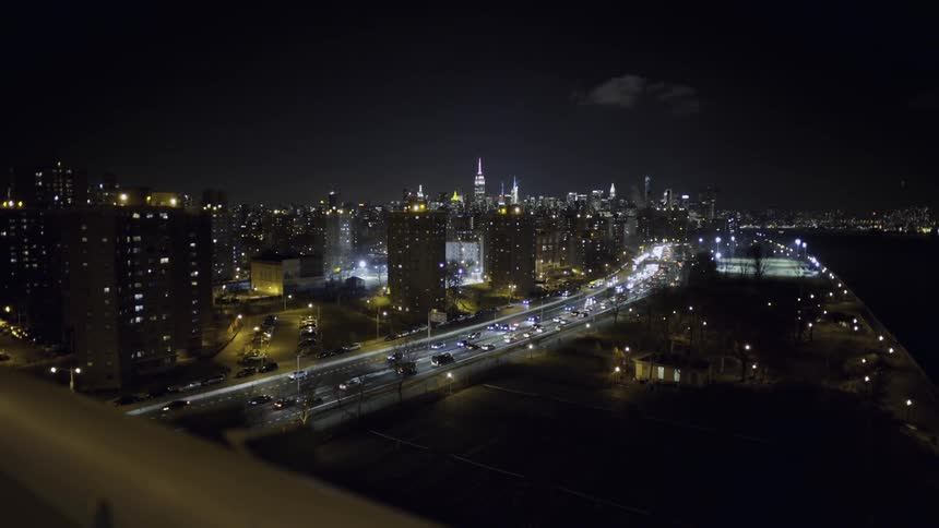 Bridge view of many vehicles travelling down a highway into a city at night