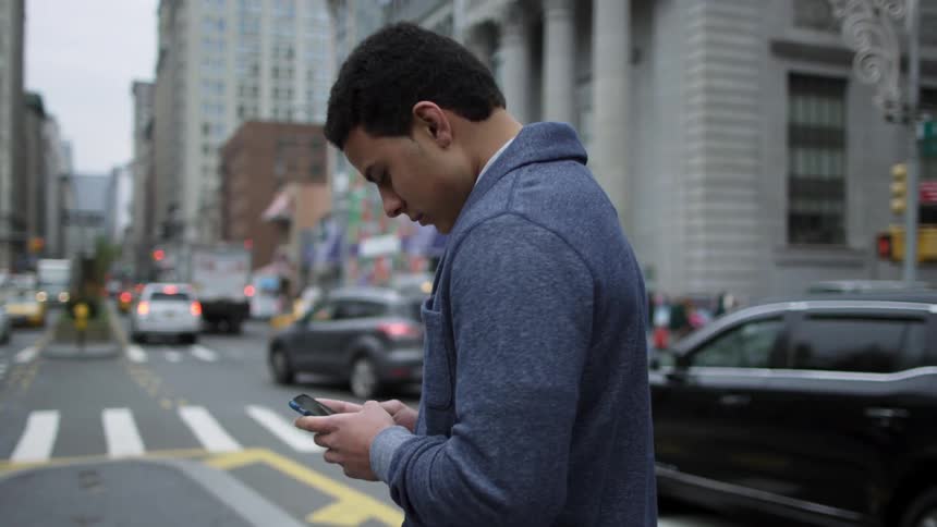 A man standing on a street boulevard typing on phone